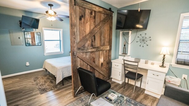 A room with a bed, a desk, a chair, a TV, and a ceiling fan. - Inn The Heights - Apt. 9 (Tampa)