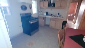 A compact kitchen with a refrigerator, stove, and cabinets. There is a dining area with a table and chairs. - Kayak Shak - Downtown Wetumpka (Wetumpka)