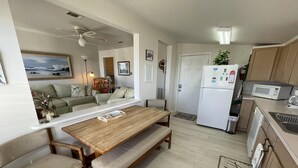 A compact kitchen with a refrigerator, microwave, and wooden dining table with benches.