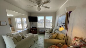 A living room with a ceiling fan, a television, and a window with blinds.