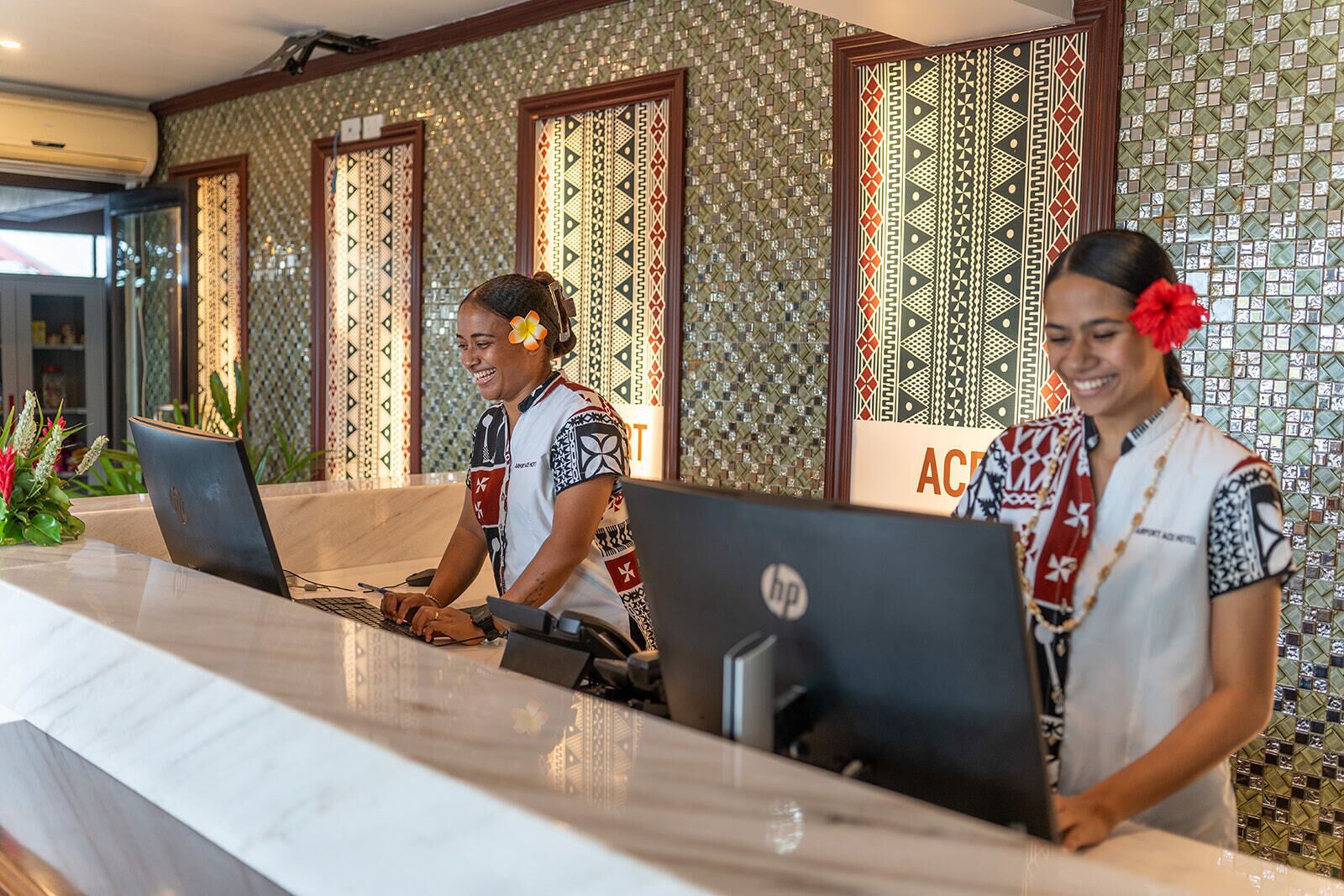 A reception desk with two employees, patterned walls, and a sign that reads "ACD".