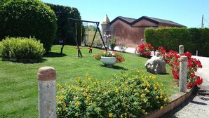 Um jardim bem cuidado com balanço, canteiro de flores amarelas e vermelhas e um caminho de pedra.