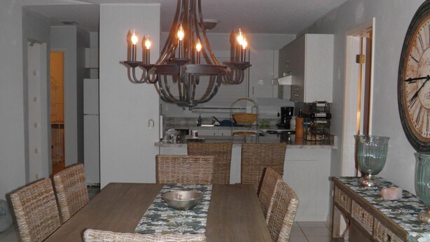 A dining area with a wooden table and wicker chairs, a chandelier, and a clock on the wall. - Salt Water Canal home w/Dock, Family/Pet Friendly, close to Beach and A1A (Palm Coast)