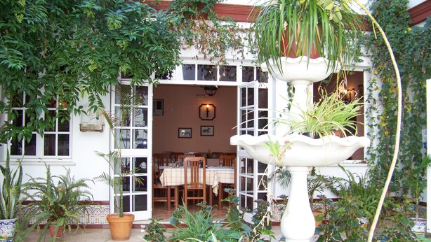 A courtyard with a dining area, potted plants, and a white fountain. - Hostal Restaurante el Lirio (Bollullos Par del Condado)