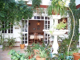 Un patio con zona de comedor, plantas en macetas y una fuente blanca.