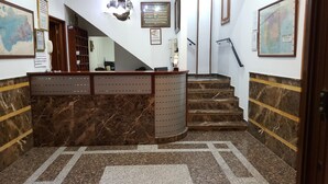 A reception desk with a marble counter, a staircase with a handrail, and a wall with framed maps and a Wi-Fi sign. - Hostal Restaurante el Lirio (Bollullos Par del Condado)
