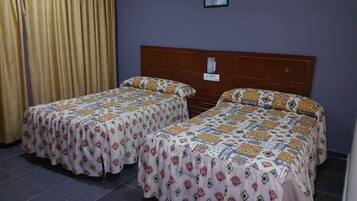 Una habitación con dos camas, cada una con una colcha estampada, cabecero de madera y una cortina a un lado.