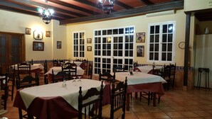 A dining area with multiple tables and chairs, large windows, and a tiled floor. - Hostal Restaurante el Lirio (Bollullos Par del Condado)