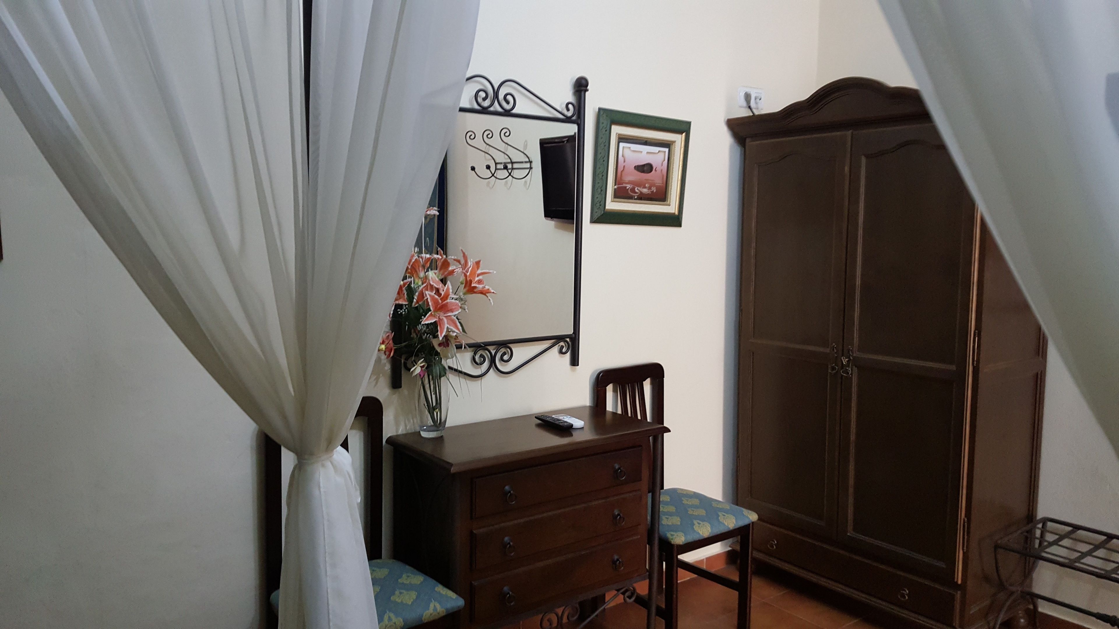 A bedroom with a wardrobe, a dresser, a chair, and a bed with white curtains.