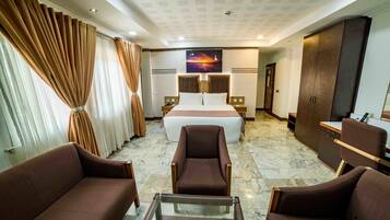 Habitación de hotel con una cama, dos sillones, un escritorio y un armario.