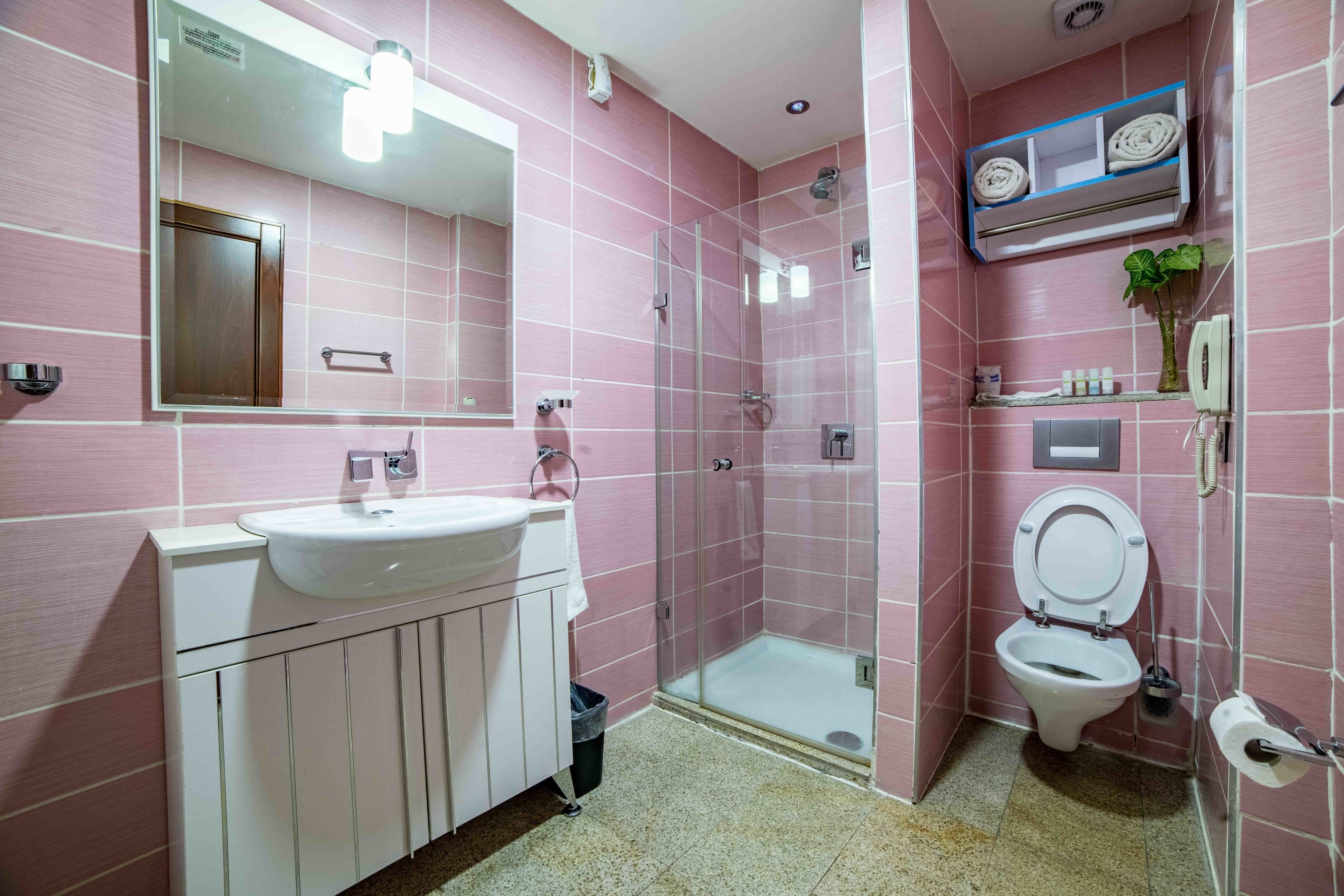 A bathroom with pink tiles, a white sink, a glass-enclosed shower, and a toilet.