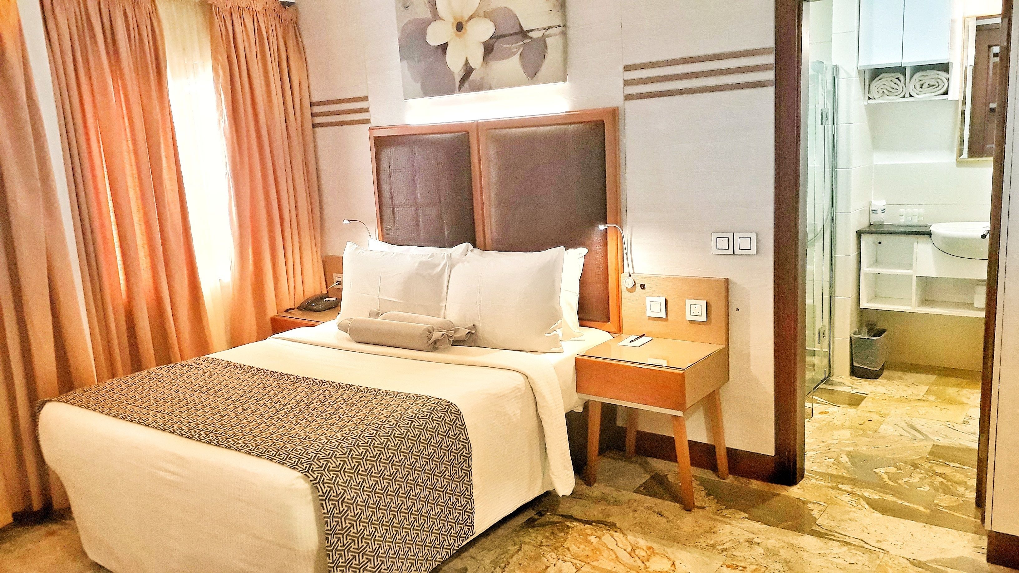 A hotel room with a bed, bedside table, lamp, and a view of the bathroom.