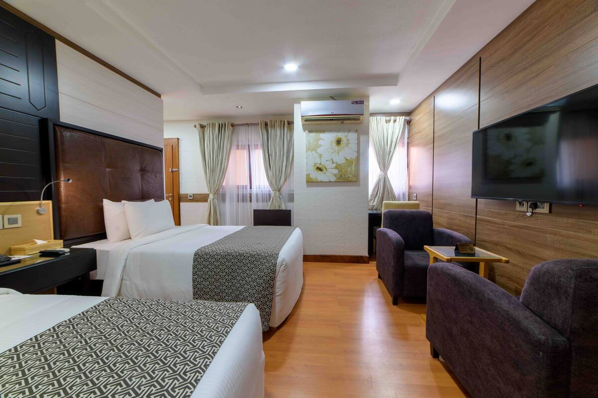 Habitació d'hotel amb dos llits, televisió, escriptori i zona de seients.