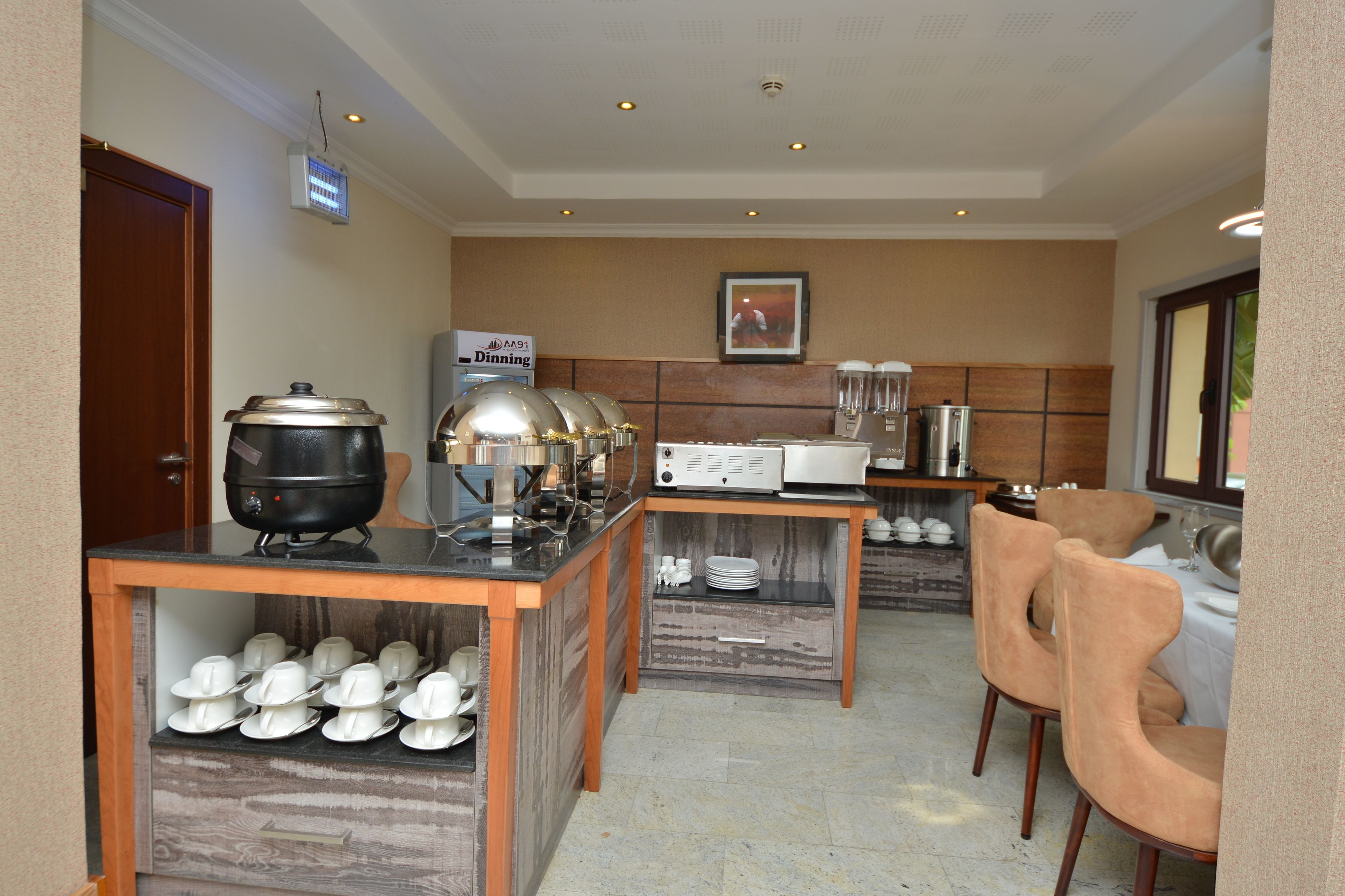 A hotel kitchen with a buffet setup, including a stove, a microwave, and a refrigerator. There are chairs and a table for dining.