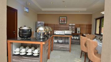 A hotel kitchen with a buffet setup, including a stove, a microwave, and a refrigerator. There are chairs and a table for dining.