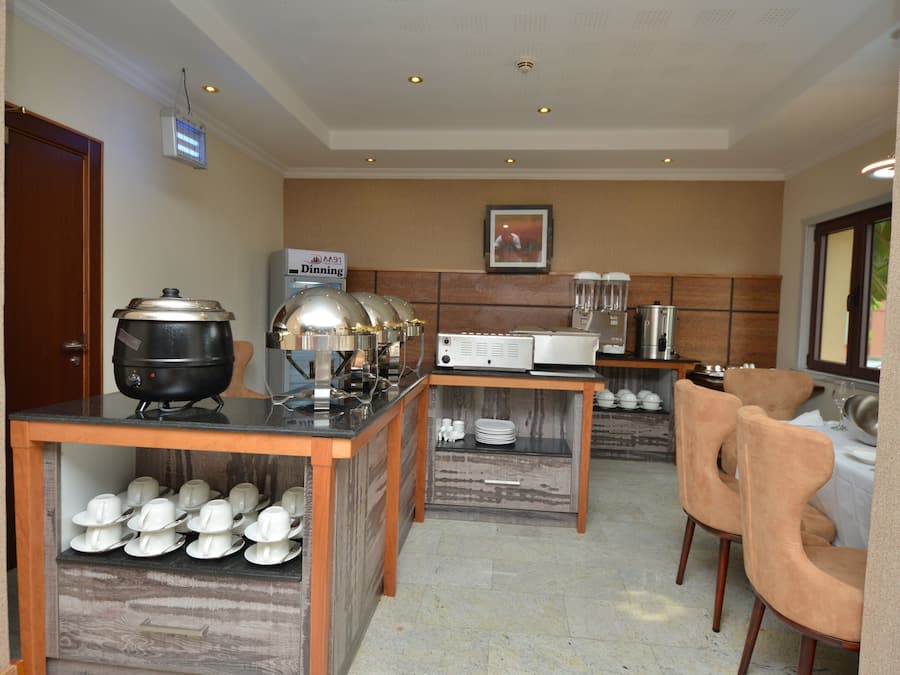 A hotel kitchen with a buffet setup, including a stove, a microwave, and a refrigerator. There are chairs and a table for dining.