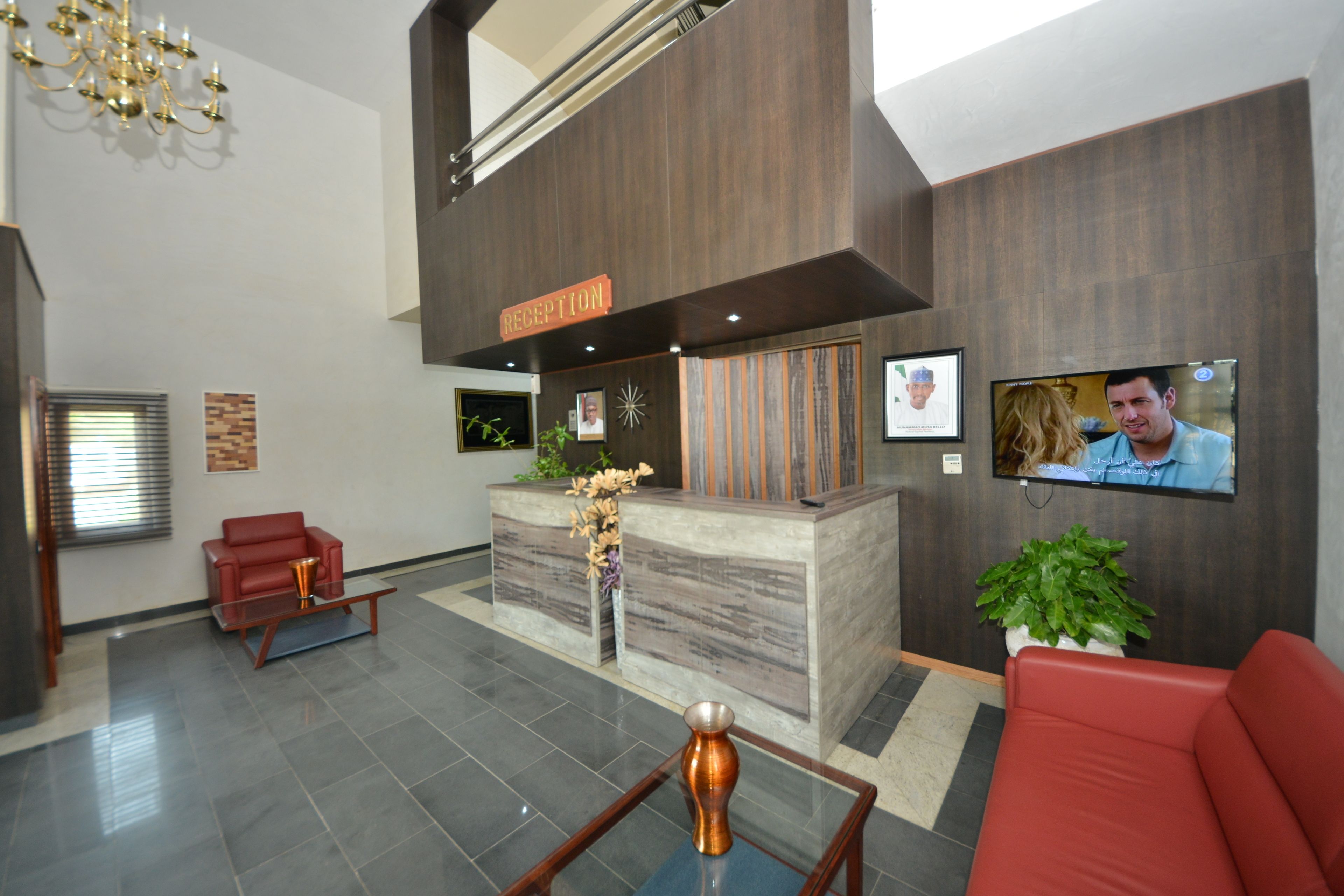 A reception area with a reception desk, a red sofa, a TV screen, and a chandelier.