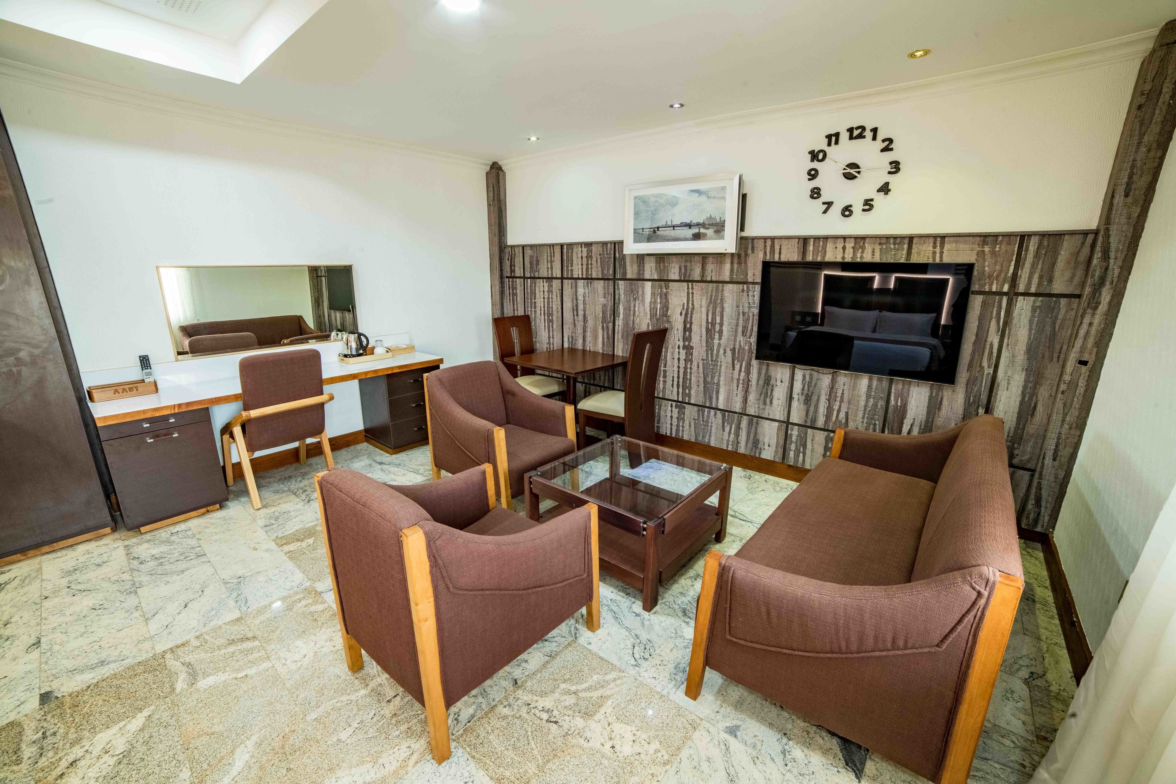 Un salon moderne comprenant un canapé, des fauteuils, une table basse, un bureau et un téléviseur fixé au mur.