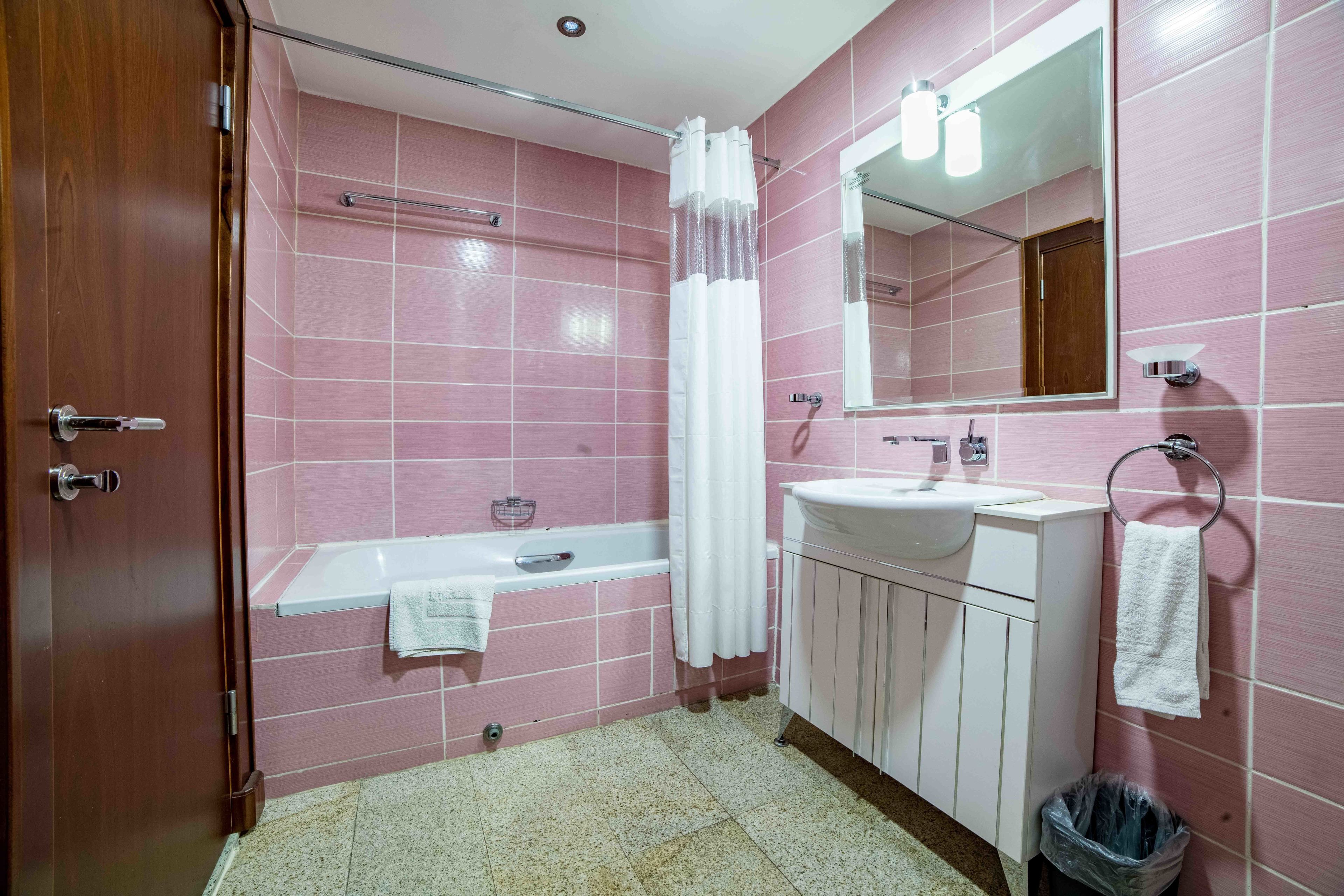 A bathroom with pink tiles, a white bathtub, a sink with a mirror, and a towel rack.