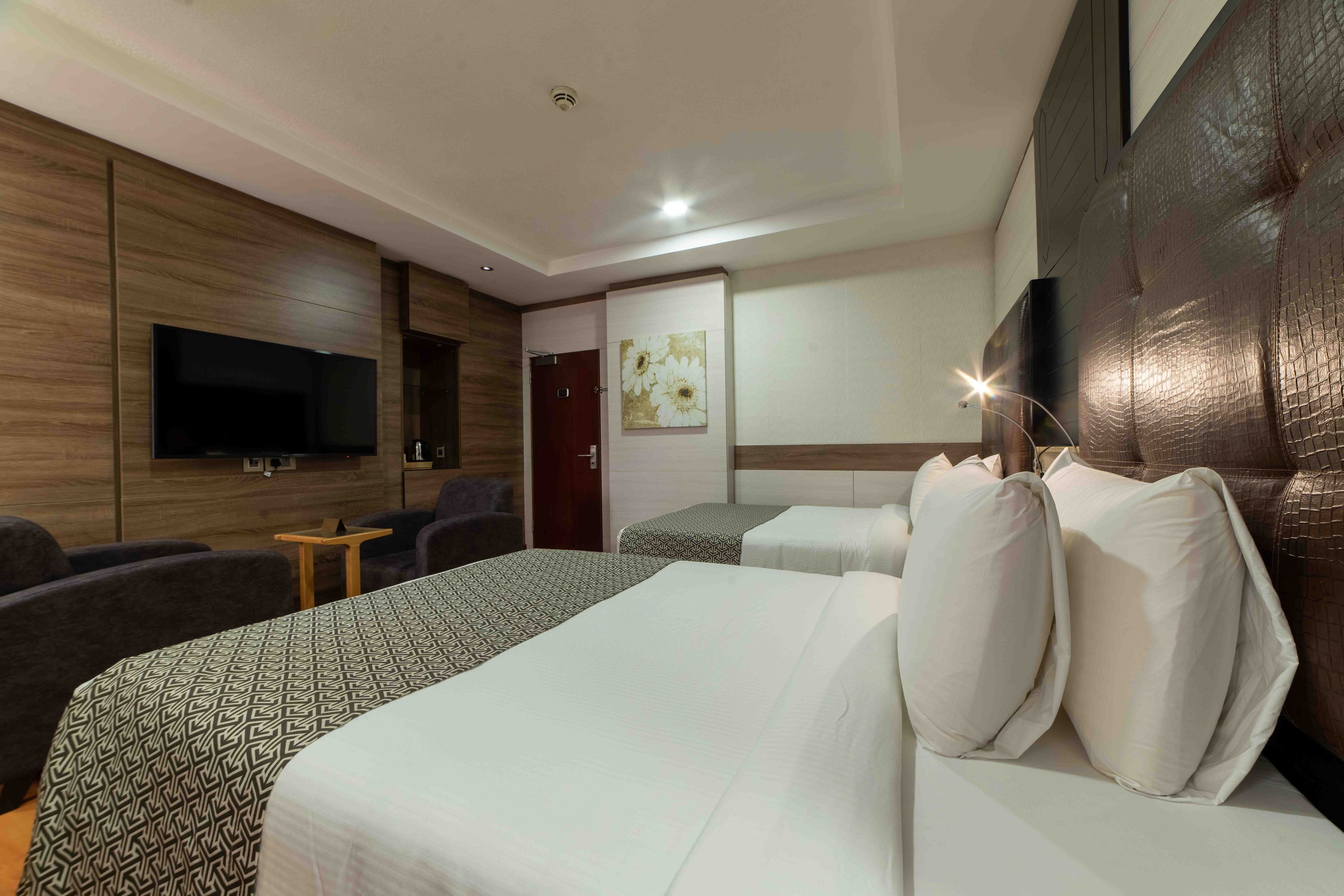 A hotel room with a large bed, two smaller beds, a flat-screen TV, a small table, and a sofa.