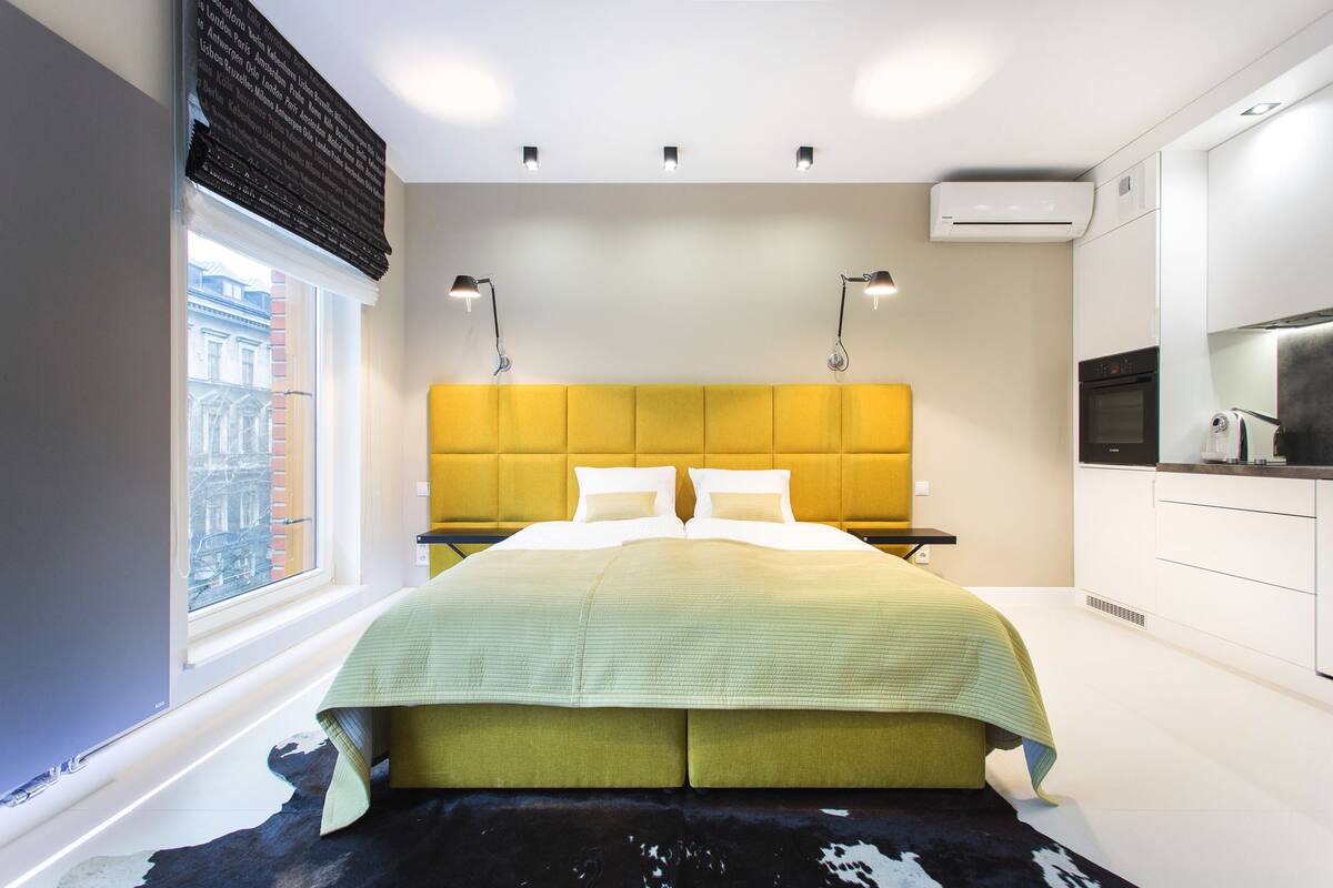 A modern bedroom with a large bed, a window with a view, and a kitchenette area.