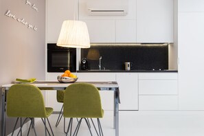 A modern kitchen with white cabinets, a black countertop, a stainless steel sink, and a bowl of oranges on the table.