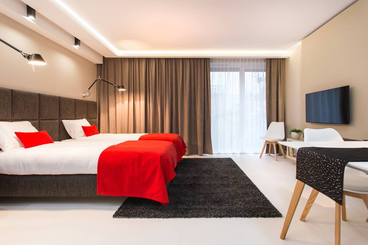 A modern hotel room with a large bed, two bedside tables, a desk, and a TV.