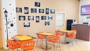 Un'aula con sedie e tavoli arancioni, uno schermo per proiettore e fotografie in bianco e nero alle pareti.