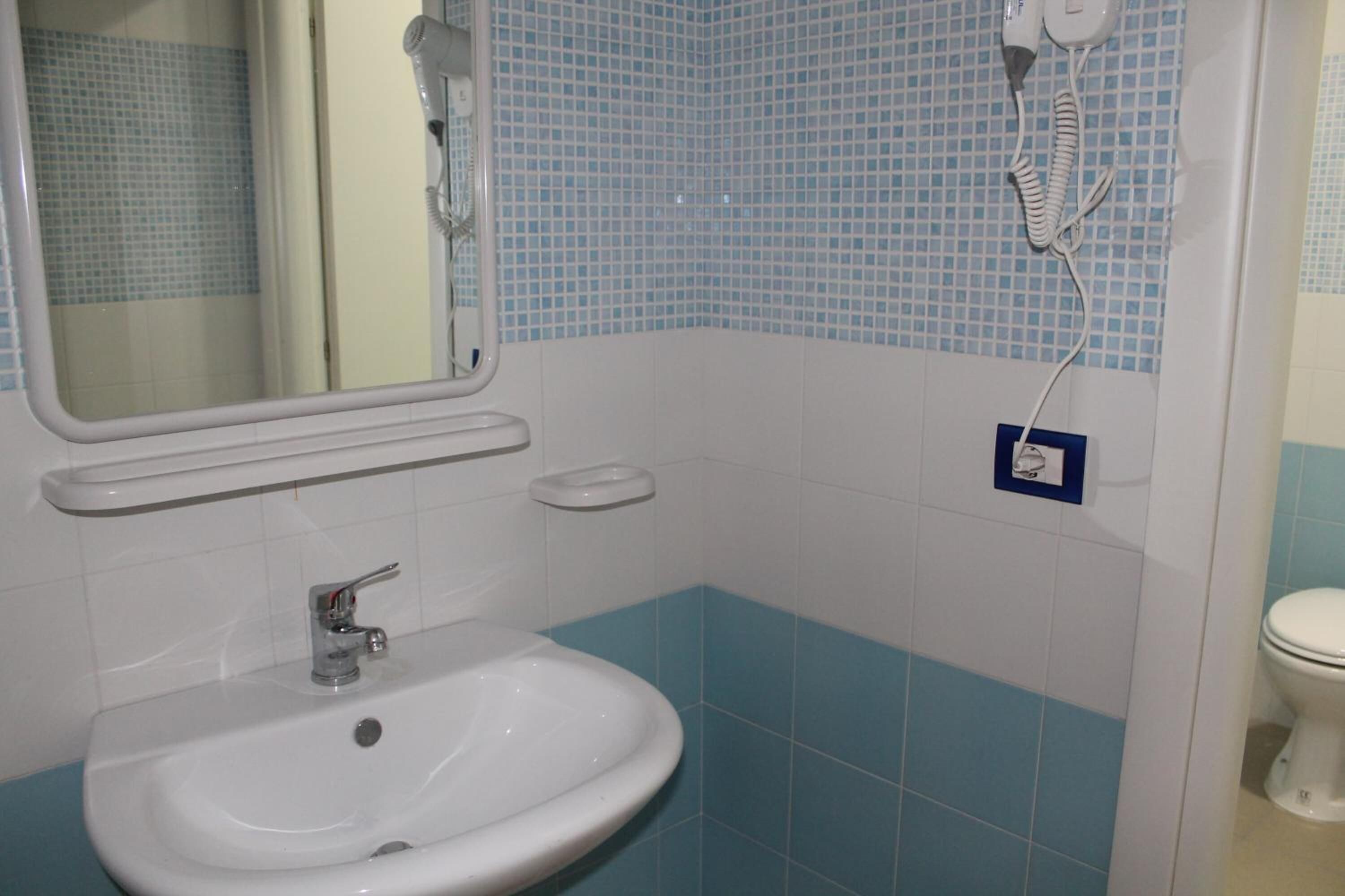 A bathroom with a sink, mirror, and a hairdryer on the wall.