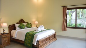 A neatly made bed with a wooden headboard, two bedside lamps, and a window with curtains. - Villa Zukunft Babonsay (Karangasem)