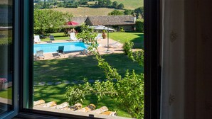 A view from a window of a swimming pool, a grassy yard, and a building with a tiled roof. - Il Raggio di Sole (Bagnoregio)