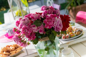 A table with a vase of pink flowers, a plate of pastries, and a glass jar.