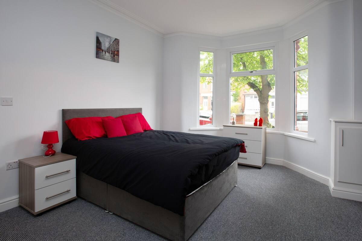 A bedroom with a bed, nightstands, a lamp, a window, and a small cabinet.