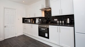 A modern kitchen with white cabinets, a black countertop, a microwave, a stove, and a built-in oven. - Crewe Rooms Ruskin Road (Crewe)