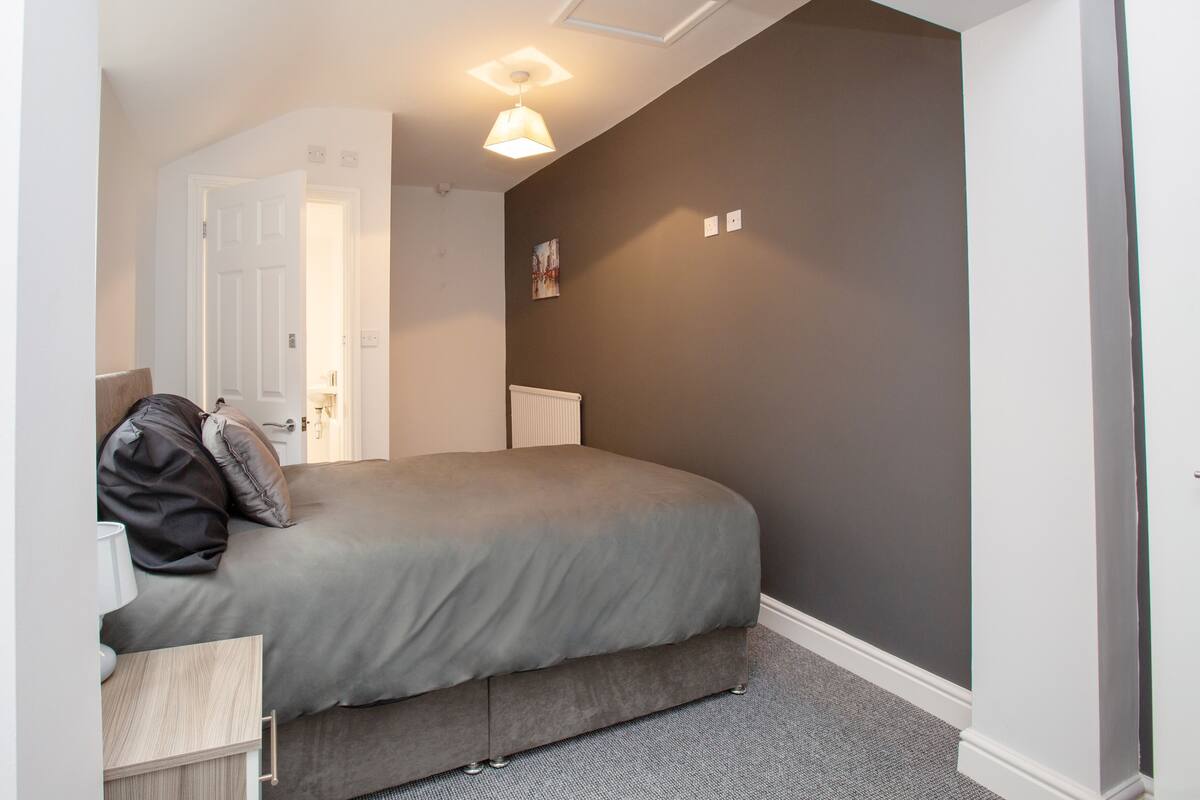 A bedroom with a bed, a bedside table, a radiator, and a door.