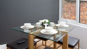 A modern dining area with a glass table, black cushioned benches, and white plates and bowls. - Crewe Rooms Ruskin Road (Crewe)