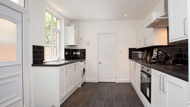 A modern kitchen with white cabinets, a black countertop, a built-in oven, and a microwave. - Crewe Rooms Ruskin Road (Crewe)