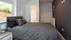 A bedroom with a bed, bedside table, lamp, and a window. - Crewe Rooms Ruskin Road (Crewe)