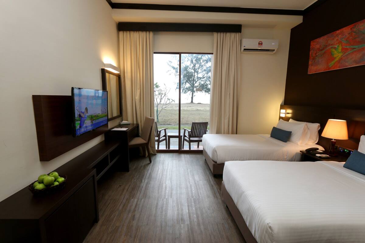 A hotel room with two beds, a TV, a desk, and a view of the outdoors.