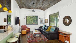 Un salon moderne avec un canapé en cuir noir, des coussins colorés, une table basse en bois et un tapis aux couleurs vives.