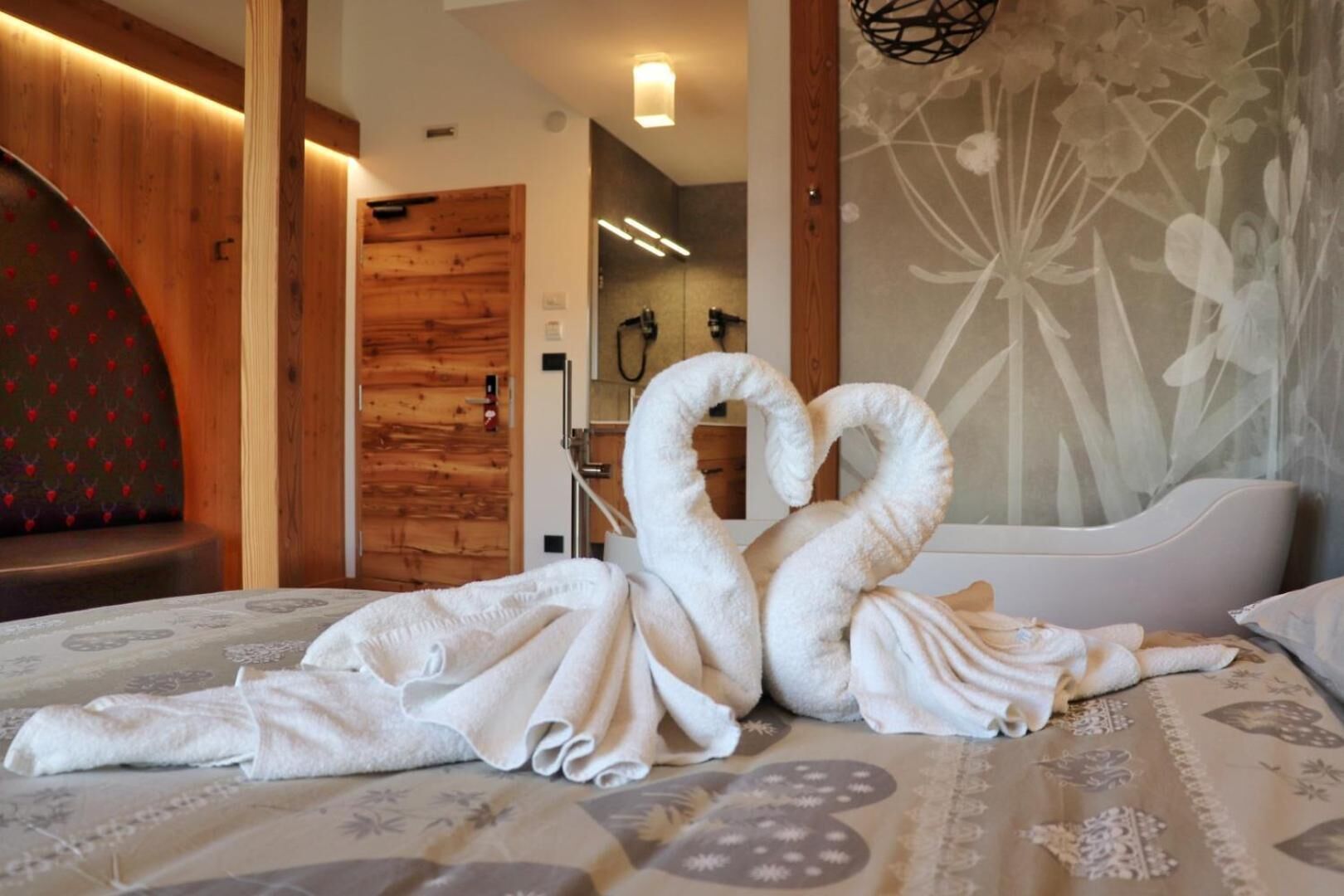 Una camera d'albergo con un letto, una porta in legno, uno spazio doccia e una parete con motivo floreale.