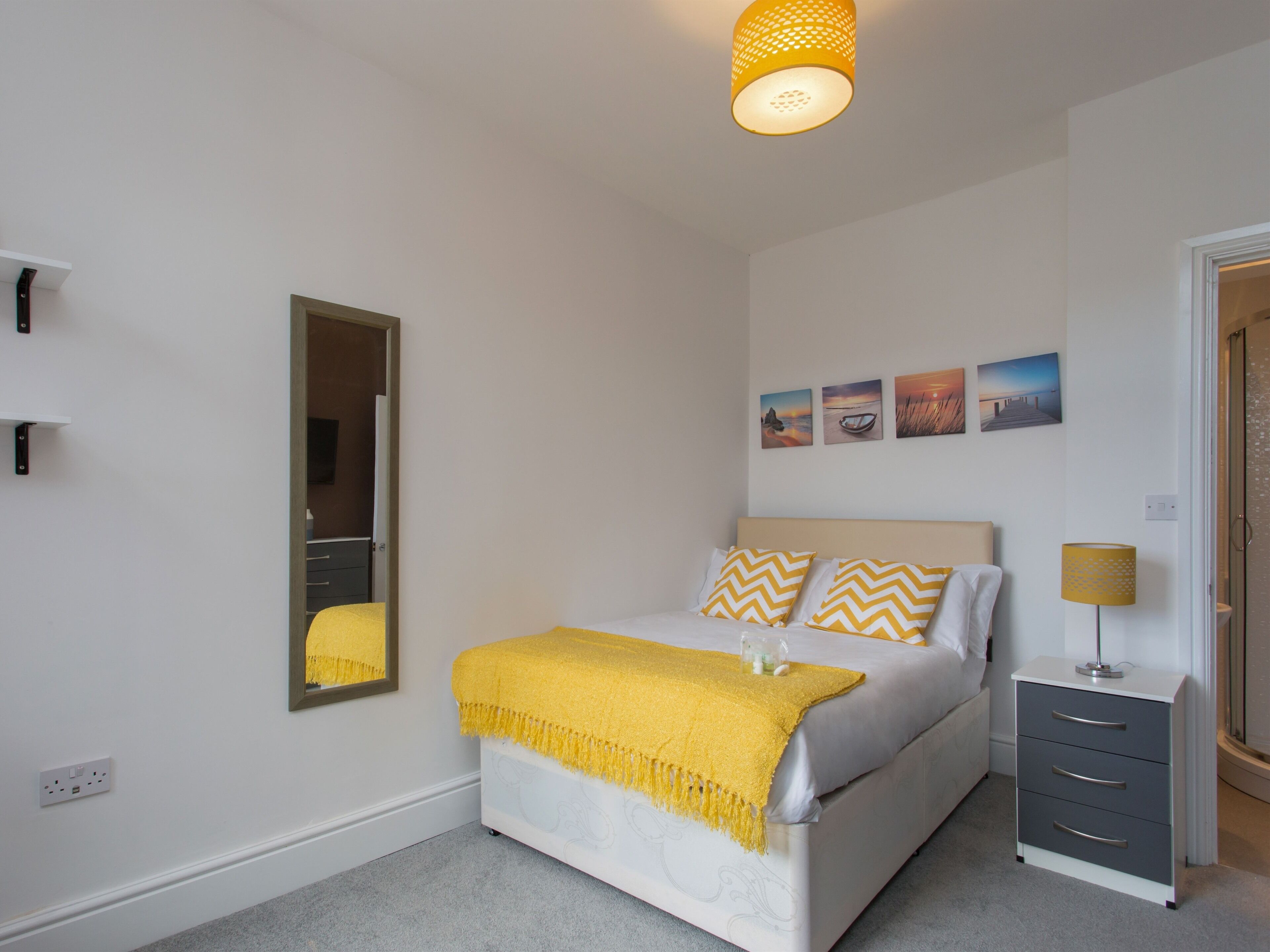 A bedroom with a bed, a bedside table, a mirror, and a wall with four pictures.