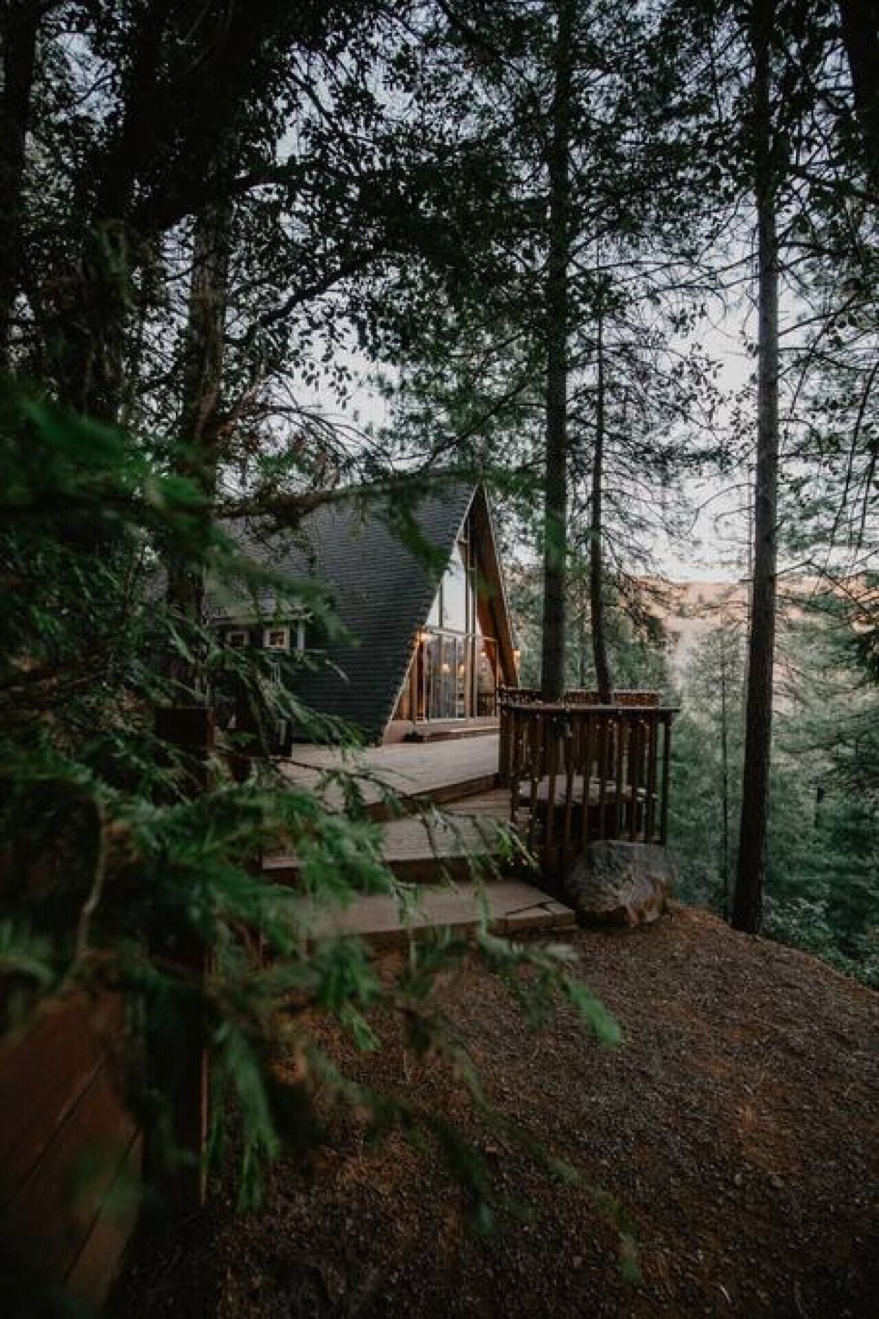 A cabin with a sloped roof, surrounded by tall trees and a wooden deck.