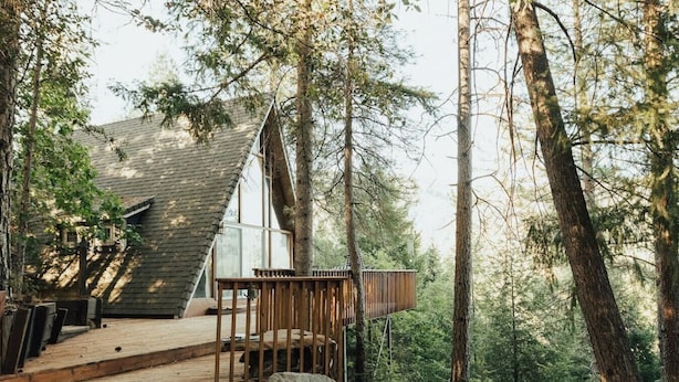 A cabin with a wooden deck and a glass balcony, surrounded by tall trees.