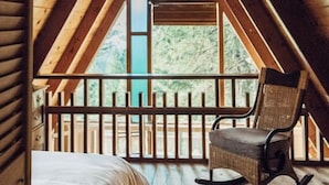 A cozy attic bedroom with a wooden sloped ceiling, a large window, and a rocking chair.