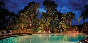 A pool surrounded by tropical vegetation and palm trees at dusk.