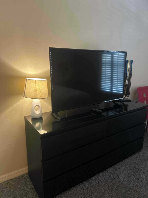 A black TV on a black dresser with a lamp on the dresser.