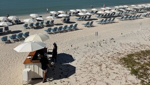 A beach with rows of sun loungers and umbrellas, a lifeguard stand, and a clear view of the ocean. - Luxury Beach Club- chairs, umbrellas, wifi, shelter included/ Pool, pickleball (Bonita Springs)