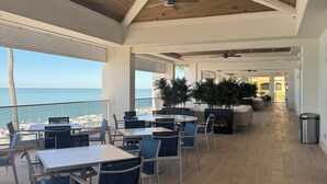 A spacious indoor area with ceiling fans, wooden flooring, and tables and chairs arranged for dining. - Luxury Beach Club- chairs, umbrellas, wifi, shelter included/ Pool, pickleball (Bonita Springs)