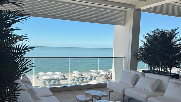 A spacious balcony with a view of the sea, furnished with white sofas and small tables. - Luxury Beach Club- chairs, umbrellas, wifi, shelter included/ Pool, pickleball (Bonita Springs)